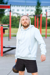 A man with an interesting braid hairstyle in a blue hoodie works out early in the morning on the street and lifts a kettlebell.