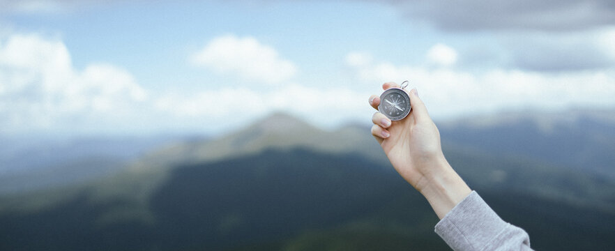 Traveler hand holds a compass in the mountains. Discover direction. Horizontal banner with place for text