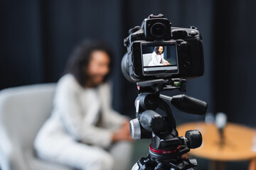 digital camera on tripod with african american journalist sitting in armchair on screen