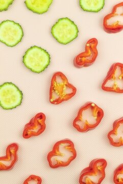 On a pink background, sliced cucumber and chopped red pepper