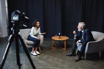 Obraz na płótnie Canvas african american journalist talking with guest in interview studio