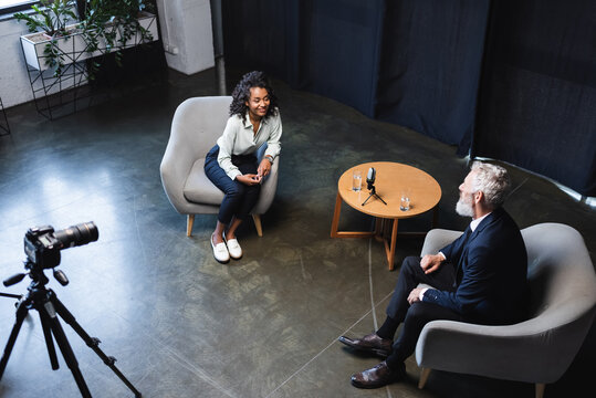 high angle view of happy african american journalist talking with guest in interview studio