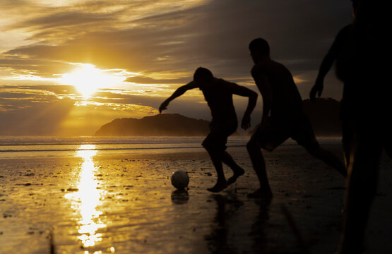 Man Kicking Soccer ball on Beach during game 