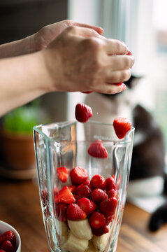 Woman adding strawberries to blender for healthy smoothie