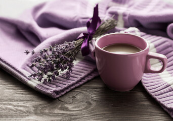 Morning coffee. A cup of coffee on a warm sweater on the background of a bouquet of flowers. Still life in lavender color. Cozy morning.
