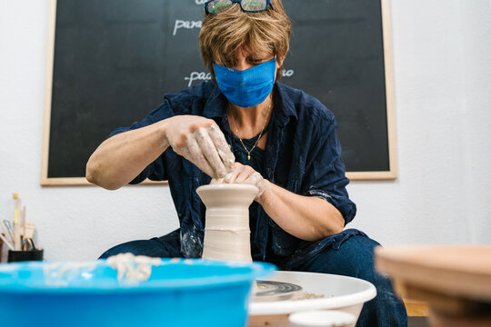 Mature ceramist with mask working at the potter's wheel