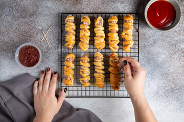 Halloween mummy hot dogs. Sausages with eyes wrapped in dough on cooling rack on concrete...