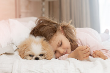 Child with baby dog. Kids play with puppy. Little girl and puppy dog sleep on bed at home. Pet at home. Animal care. Friendship between animal and children