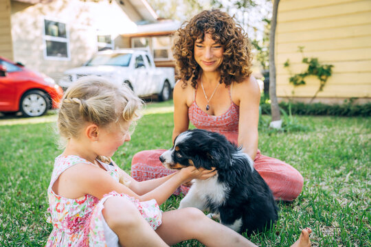 Girl and mother petting australian shepherd puppy on front lawn of home