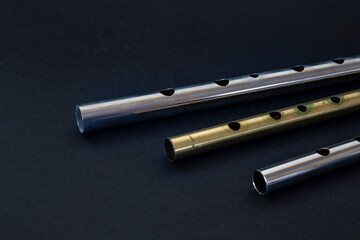 Three tin whistles, nickel and brass over black background. Close up photography.