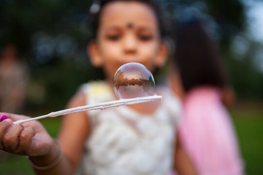 Little Indian girl looking at soap bubbles at outdoors
