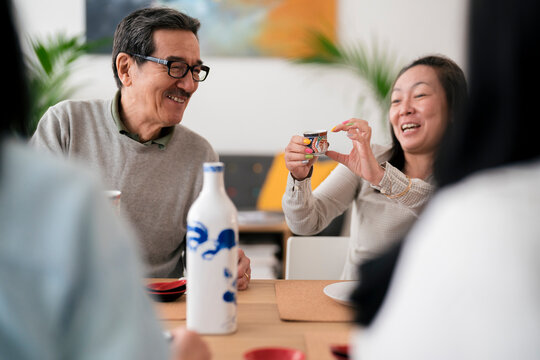 Company of cheerful Asian friends dinking sake at home