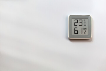 Electronic indoor gray plastic digital thermometer on white wall showing temperature, humidity...