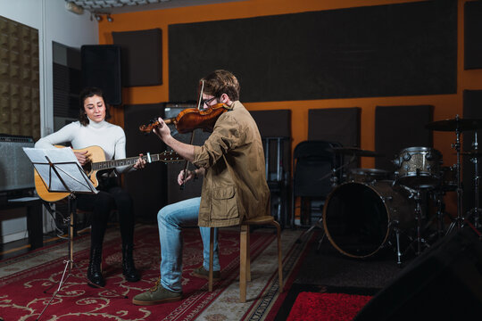 Man playing on violin near woman with guitar in studio