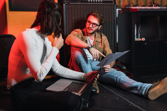 Woman near man with laptop on ground near in studio