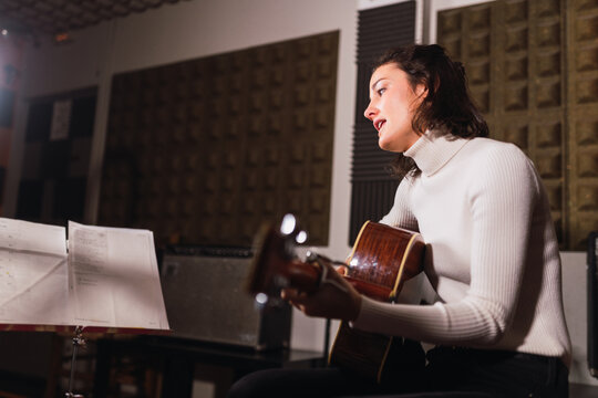 Woman playing on guitar near printed music in studio