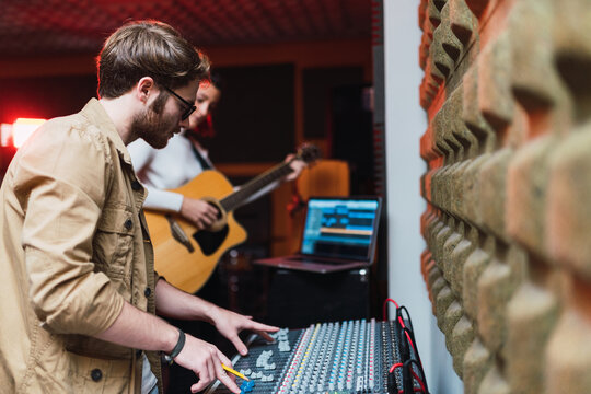 Woman playing on guitar near man using equalizer in studio