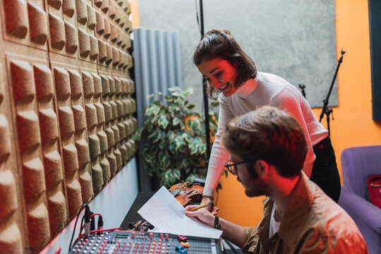 Woman near man with paper using equalizer in studio