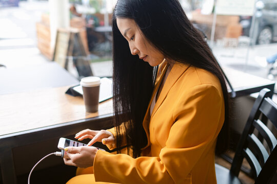 Young Chinese woman using smartphone near colleague in cafe