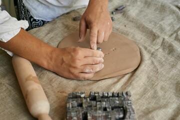 female artisan ceramist makes lettering impression on clay layer