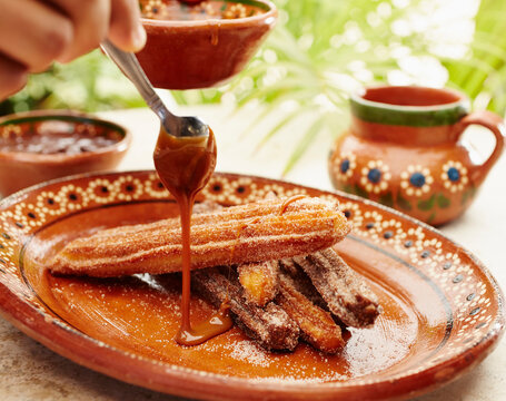 Server pouring chocolate sauce on churros dessert