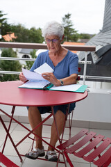An elderly woman reads written administrative documents sitting at a table