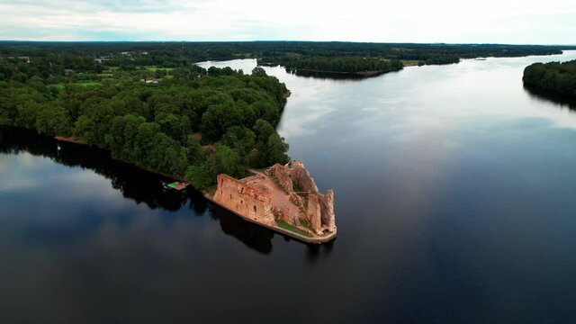 Side flight by drone near the ruins of a medieval castle in Koknese. Aerial view of a beautiful blue river, green forest and sky. Latvia, Eastern Europe.