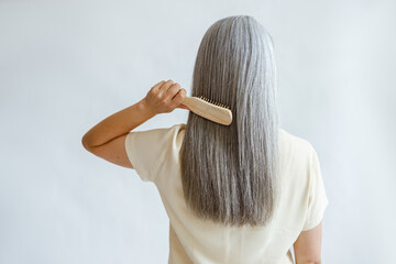 Lady in yellow blouse brushes straight silver hair standing on light grey background in studio...