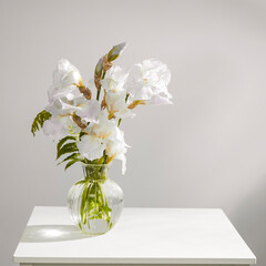 A bouquet of three white irises and a fern in a transparent vase on the table.