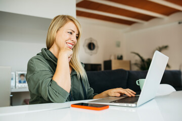 Middle age smiling blonde woman using a laptop in a livingroom