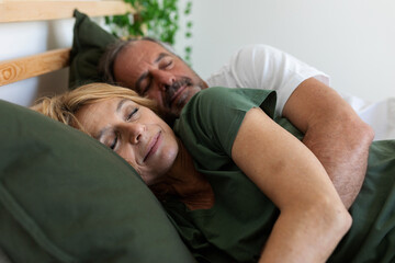 Senior married couple sleeping cuddled in bed