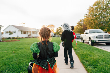 The backside of children walking down the sidewalk in cosutmes. 