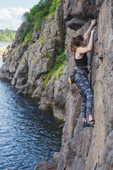 A girl climbs a rock above the water