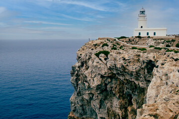 Fototapeta na wymiar Menorca, Spain View of Cavalleria lighthouse with rocky cliff during a summer day with dramatic cloudy sunset in the balearic island of Menorca in Spain