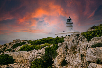 Fototapeta na wymiar View of Cavalleria lighthouse with rocky cliff during a summer day with dramatic cloudy sunset in the balearic island of Menorca in Spain