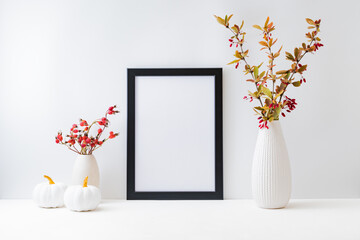 Home interior with decor elements. Mockup with a black frame, colorful autumn leaves and red berries in a vase on a light background