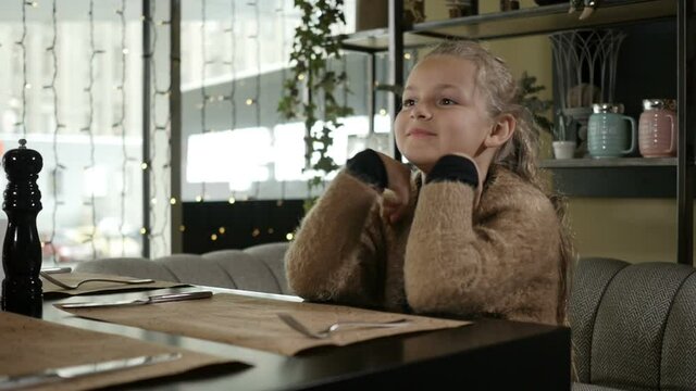 a girl with blonde hair closes her eyes with her hands sitting in a restaurant with her mother. High quality FullHD footage