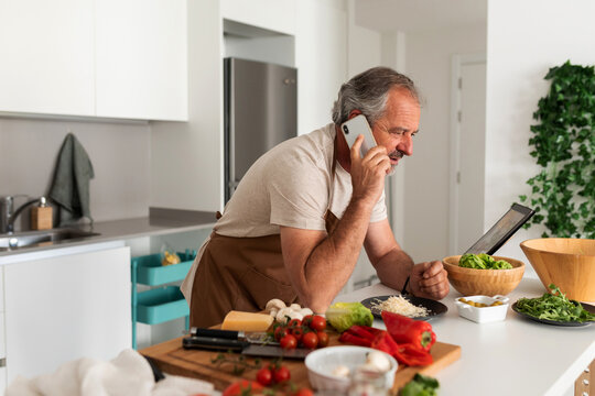 Mature Man Cooking Lunch And Calling By Phone