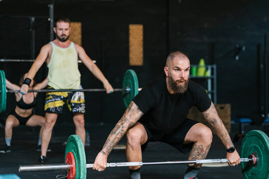 Male athlete deadlifting barbell during group workout