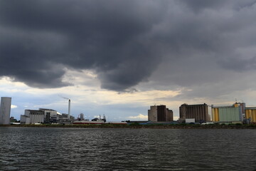 Obraz premium Industry by the water. Factory. Great and beautiful view in a far distance. Gray dark clouds in the sky. Copy space for extra text. At the Swedish lake Vänern or Vanern. Lidköping, Sweden, Europe.