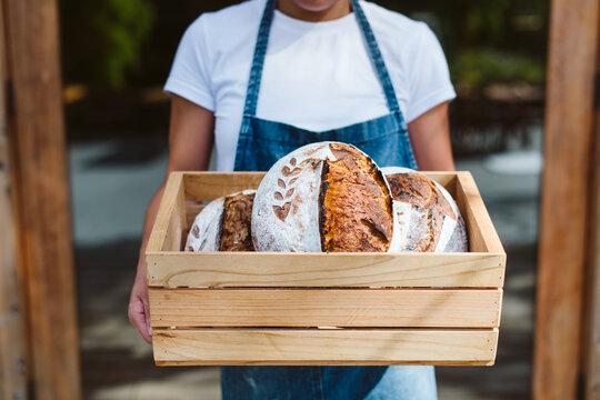 Woman holds fresh made sourdough bread in a wood crate.