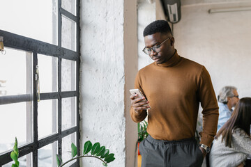 Young businessman standing next to the window in the office using phone