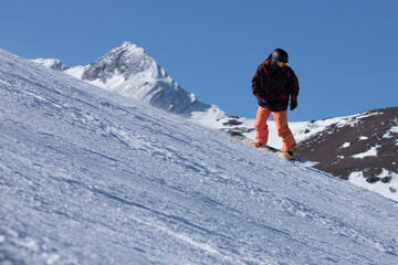 Fototapeta na wymiar A man riding a snowboard down a snow covered slope on a sunny day with snowy mountains in the background wearing a helmet
