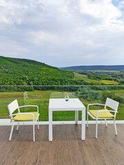 Table and two chairs with cushions on the empty balcony. White furniture on the terrace with a beautiful view of the forest in a hilly area. Background for recreational, relaxation and resting.