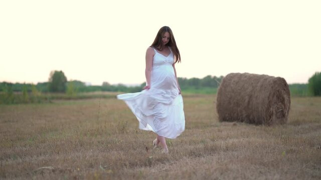 Beautiful pregnant woman in wheat field with haystacks at summer day