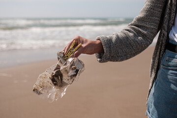 Faceless young woman cleaning the beach of plastics