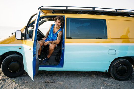 Happy adventurer sitting in camper van on beach