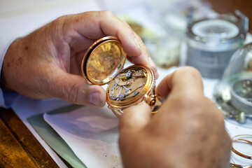 Mature Watchmaker repairing vintage pocket watch and clock on the workbench.   - obrazy, fototapety, plakaty