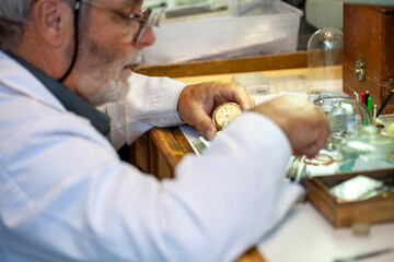 Mature Watchmaker repairing vintage pocket watch and clock on the workbench.  