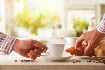 Fototapeta na wymiar Hand taking hot morning coffee on breakfast table with croissants
